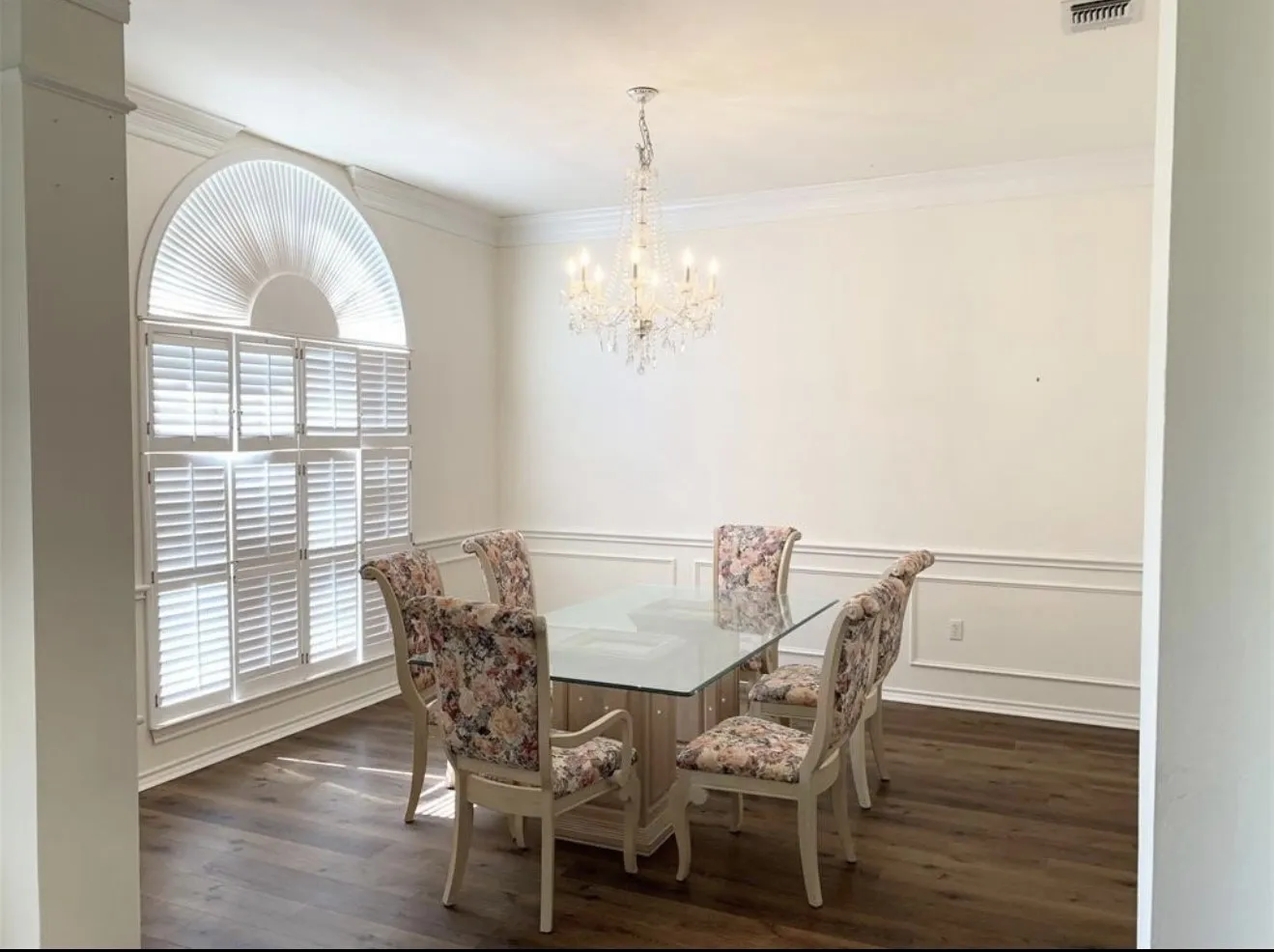 Dining area featuring wood-finish flooring, white crown molding, and wainscoting
