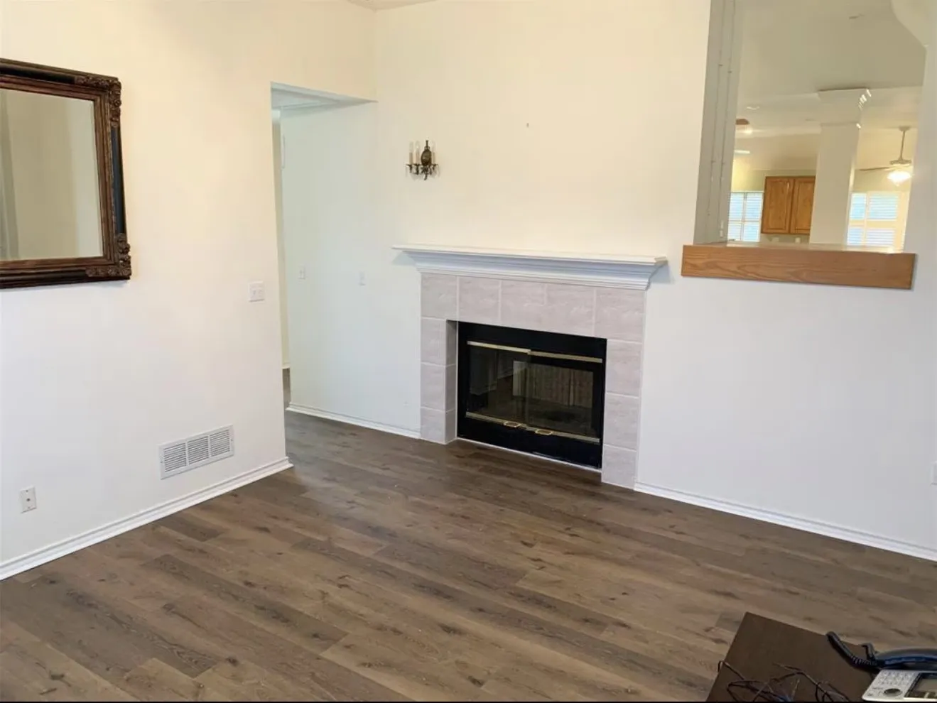 Living area featuring wood-finish flooring, a tiled fireplace with a mantel, white baseboards, and a pass-through window with a wood ledge