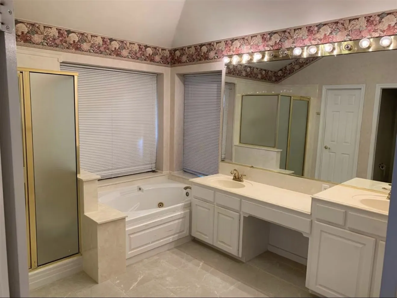 Spacious bathroom featuring an integrated jetted tub, a separate shower enclosure with gold-tone framing, and a double vanity with ample counter space