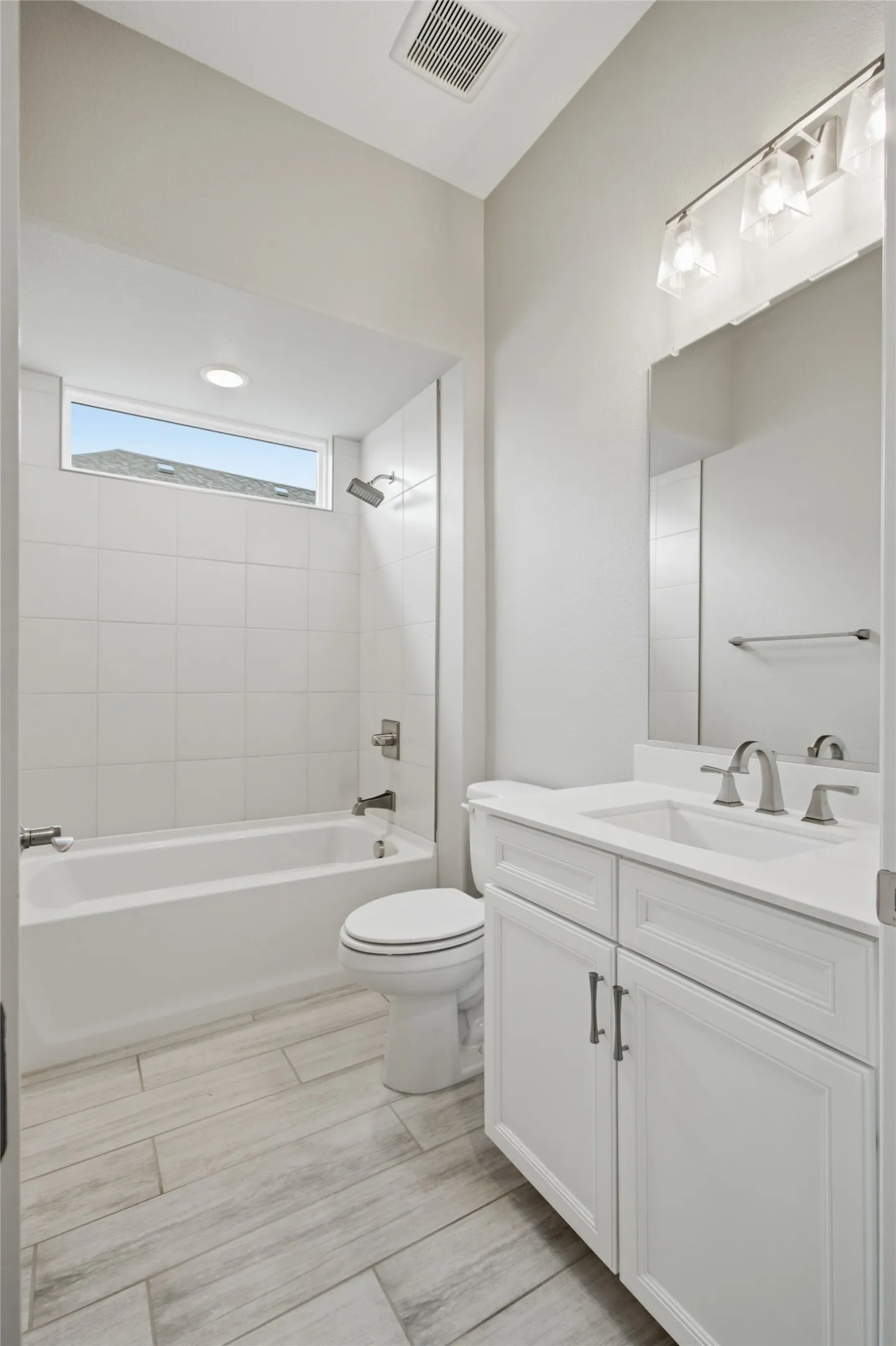 En suite bathroom for guest suite with wood-finish tile, white vanity and a tub/shower with subway tile surround plus transom window