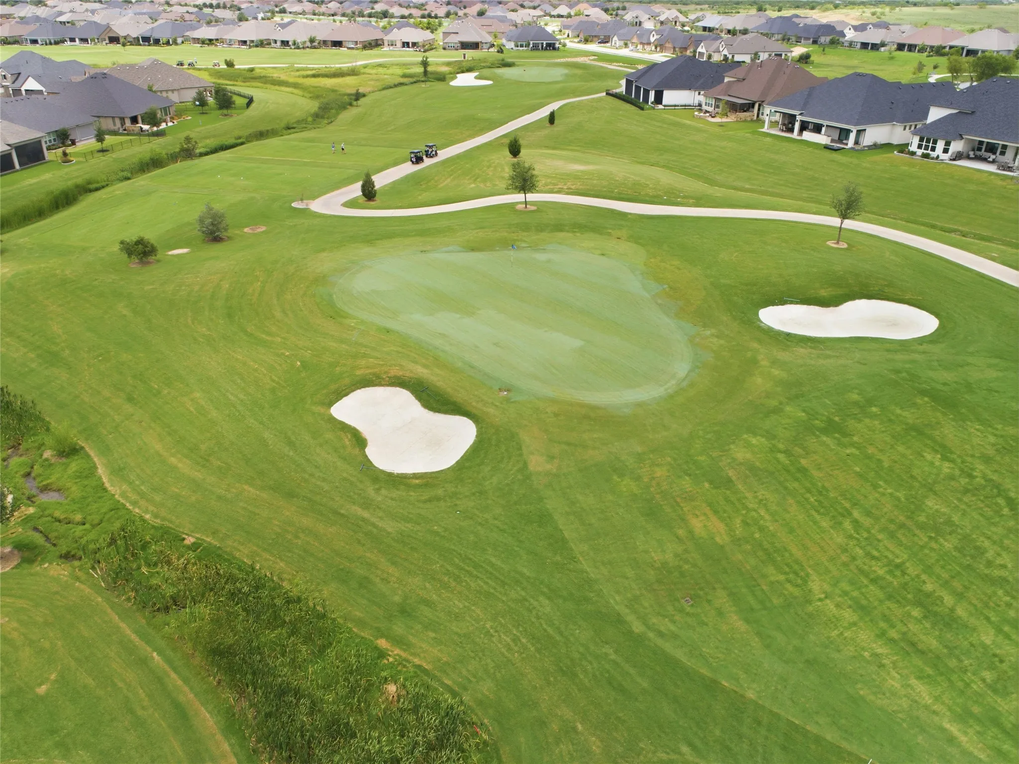 Expansive golf course featuring a green, two sand bunkers, and a paved cart path