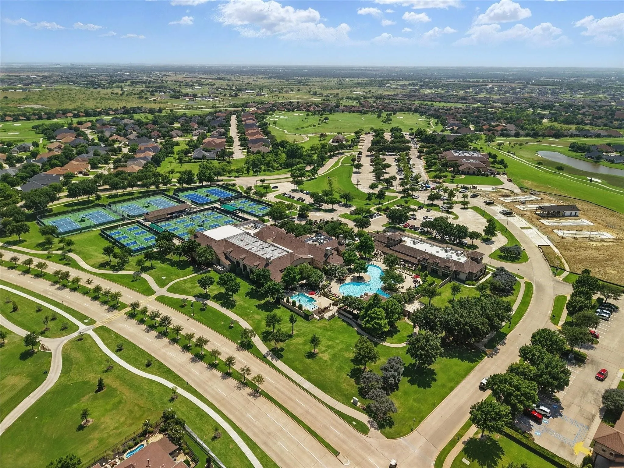 Overview of recreational facilities - tennis and pickleball courts, a large swimming pool complex, clubhouse buildings, and surrounding green spaces