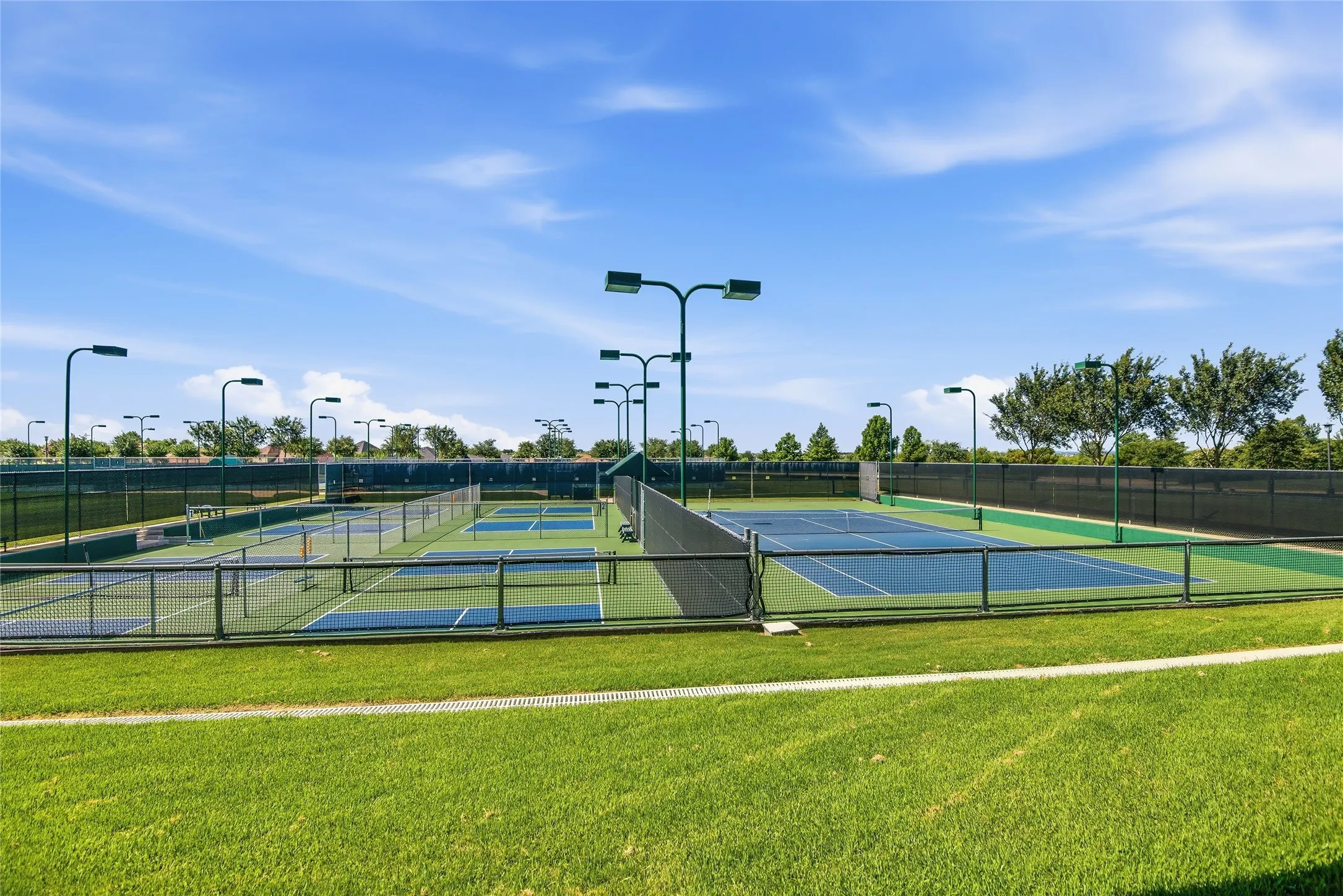 Pickleball and tennis courts featuring blue and green surfacing, surrounded by fencing and overhead lighting