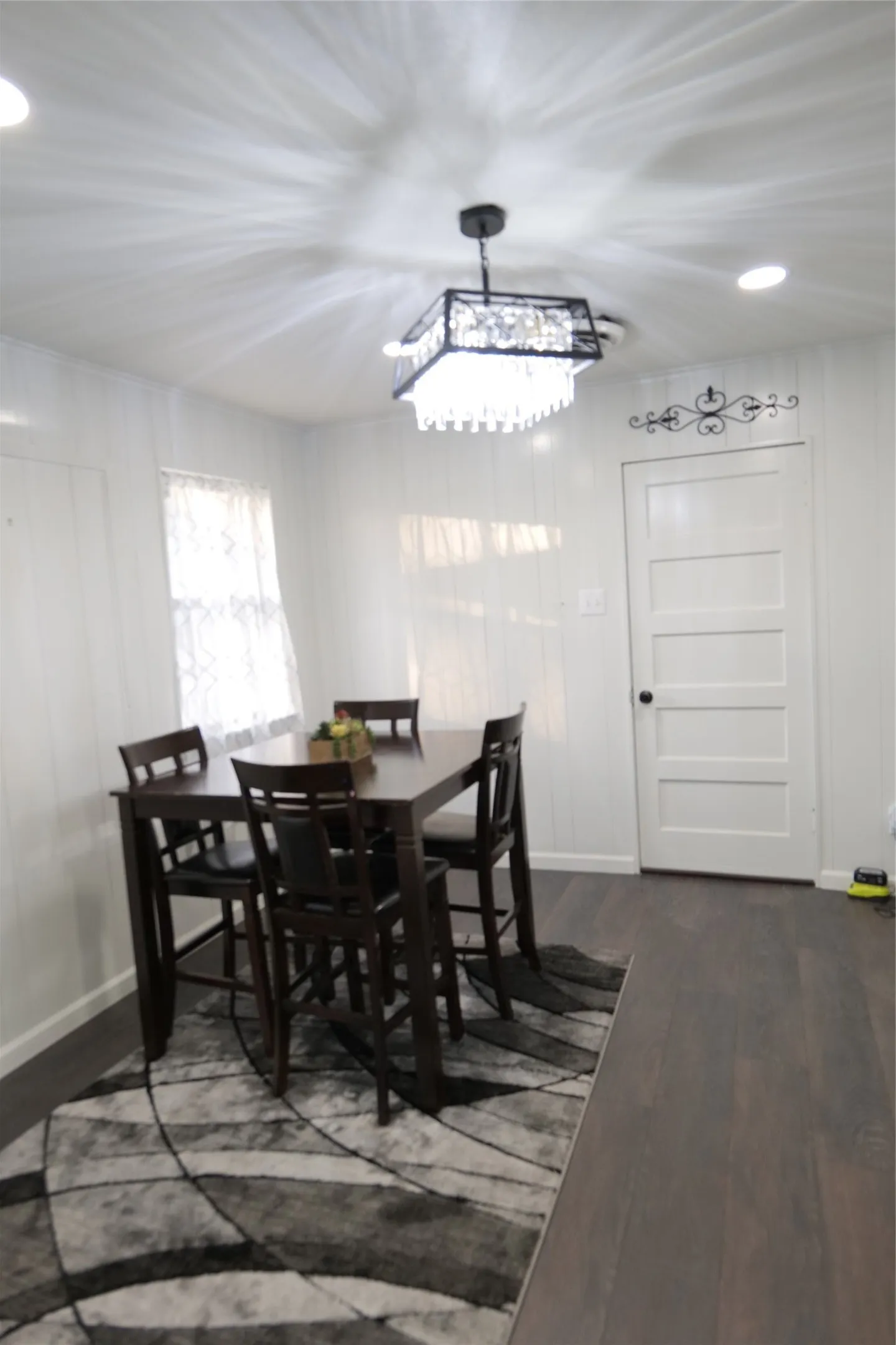 Dining area featuring wood-finish flooring, white paneled walls, and a contemporary crystal chandelier with recessed lighting
