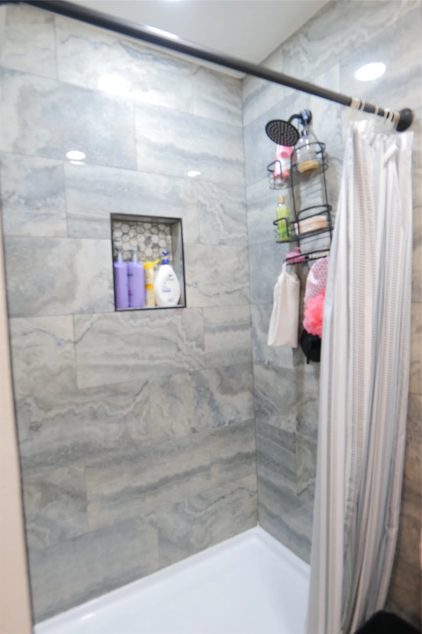 Tiled shower with a recessed niche featuring hexagonal mosaic tile, a rain shower head, and recessed lighting