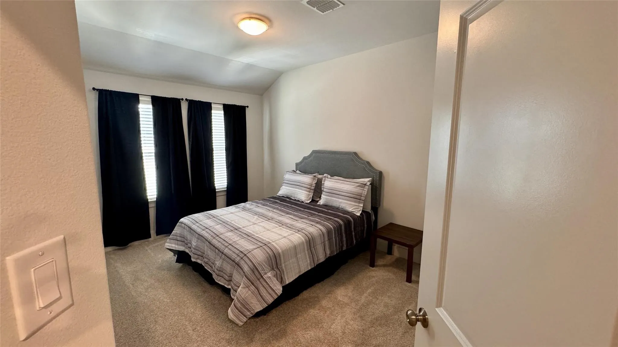 Carpeted room featuring multiple windows with blinds, a vaulted ceiling, and a flush-mount ceiling light fixture