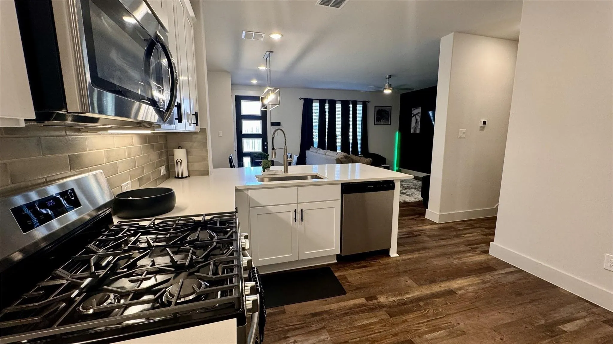 Modern kitchen featuring stainless steel appliances, white cabinetry, a large center island with an undermount sink, neutral subway tile backsplash, and wood-finish flooring