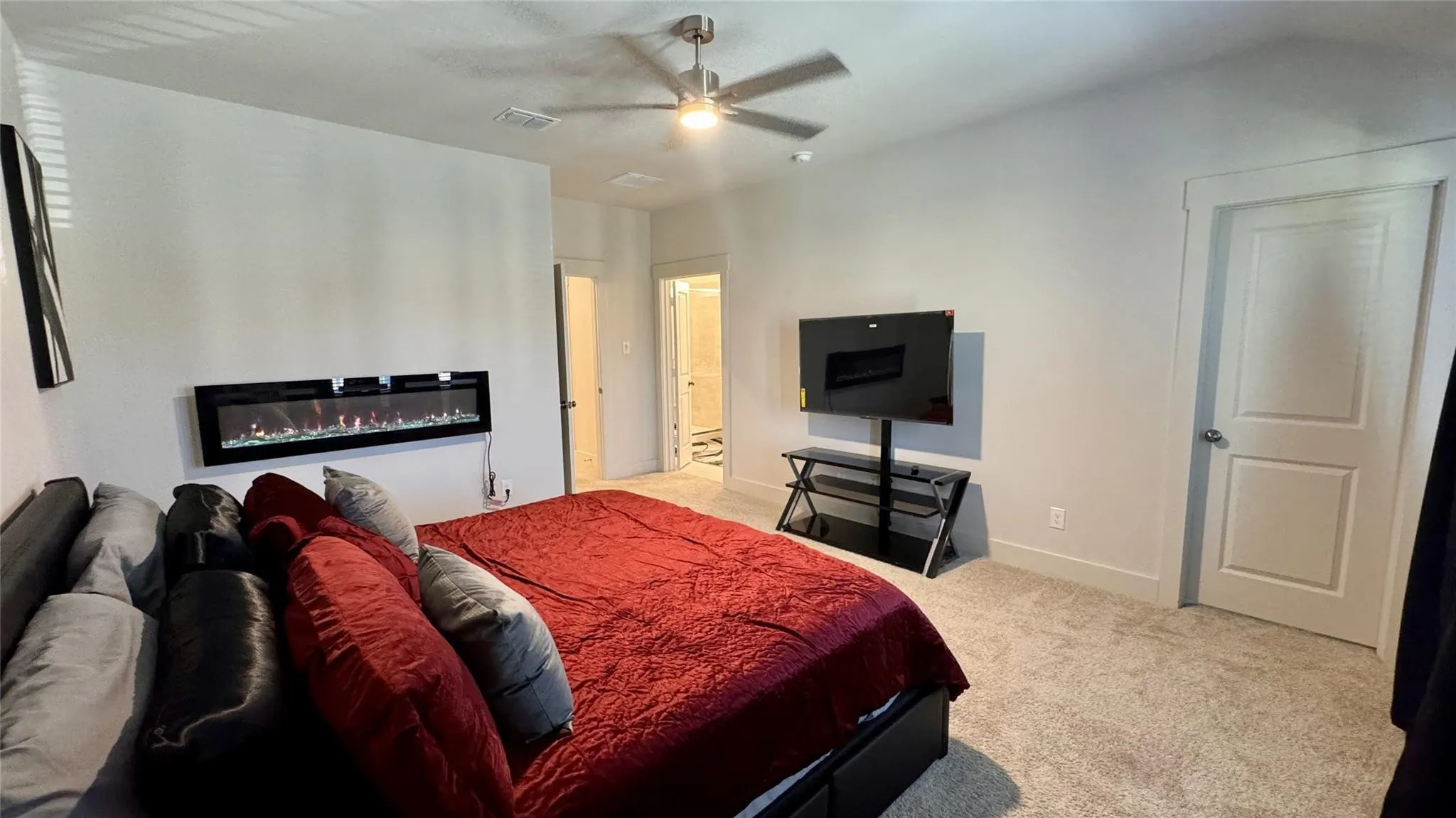 Spacious bedroom featuring an electric fireplace, light-toned carpeting, a ceiling fan, and white trim