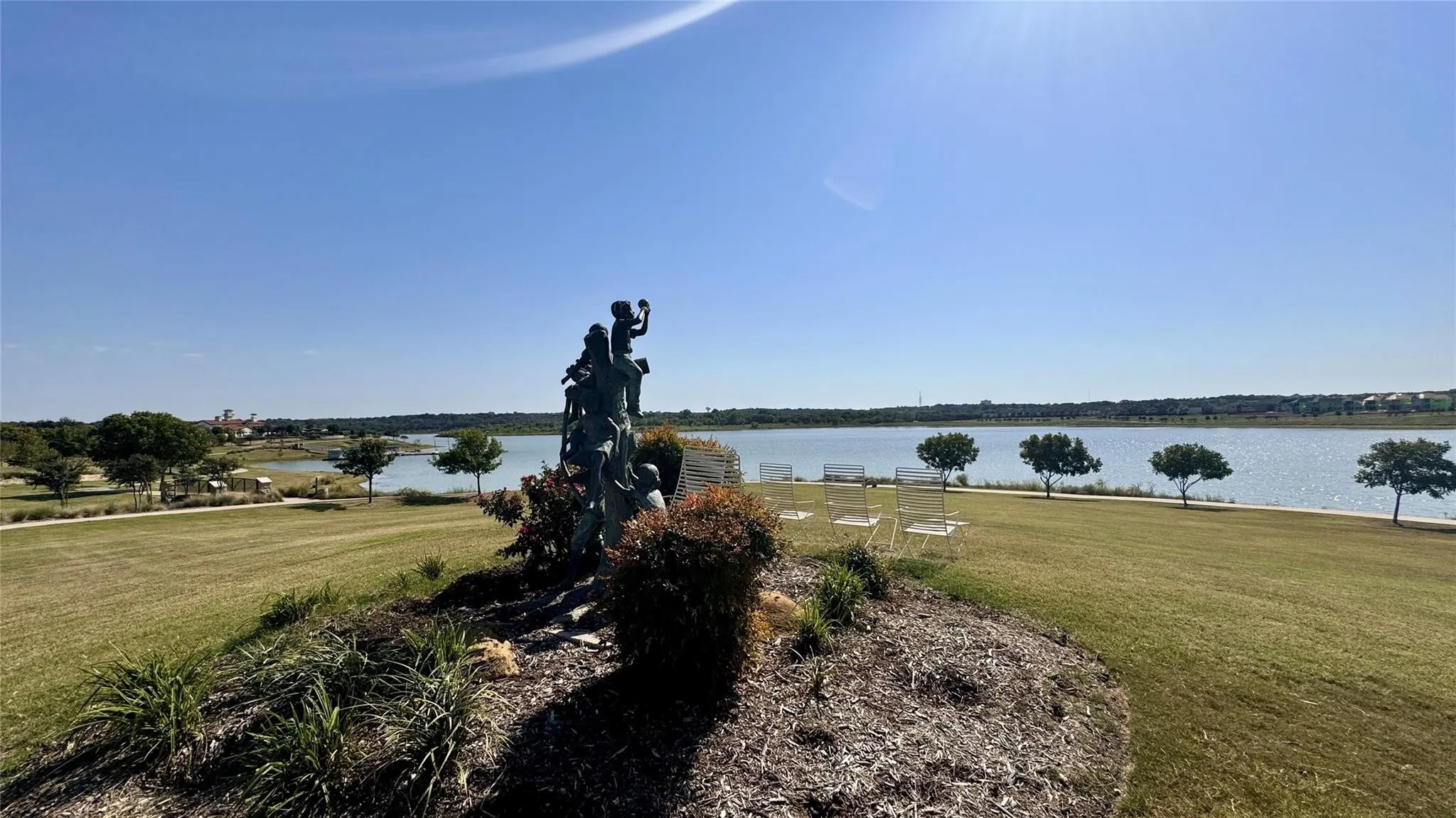 Expansive waterfront setting featuring a grassy slope, mature trees, and a decorative sculpture