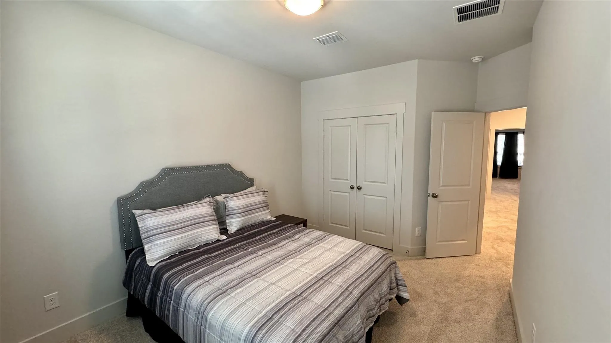 Neutral-toned bedroom featuring plush carpeting, a double-door closet with spherical hardware, and a single ceiling light fixture