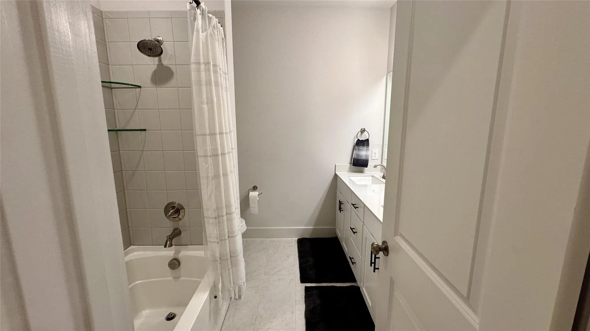 Bathroom featuring a white bathtub, tiled shower surround, and a dual-sink vanity with white countertop