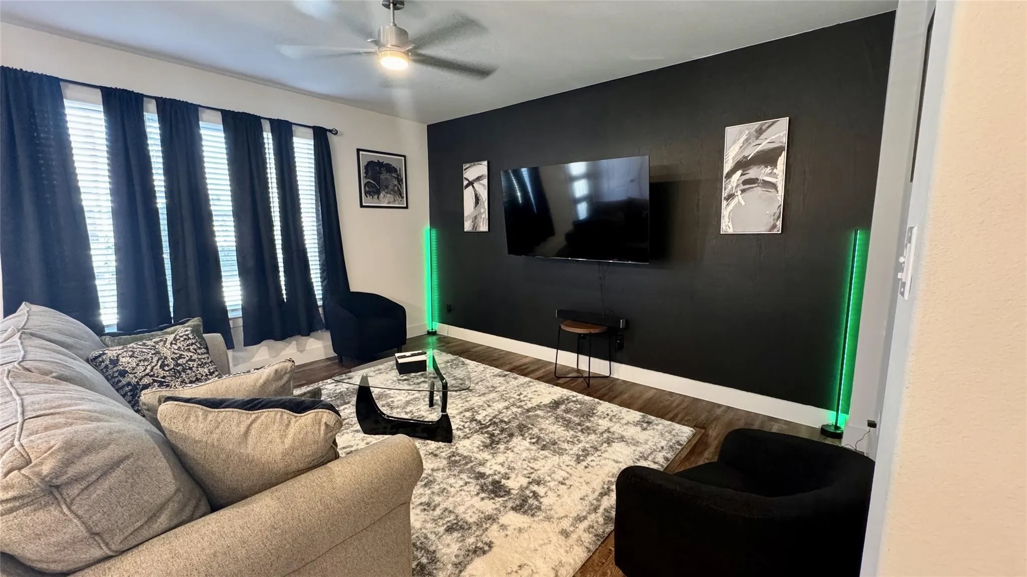 Living area featuring wood-finish flooring, a ceiling fan with integrated lighting, and a dark accent wall