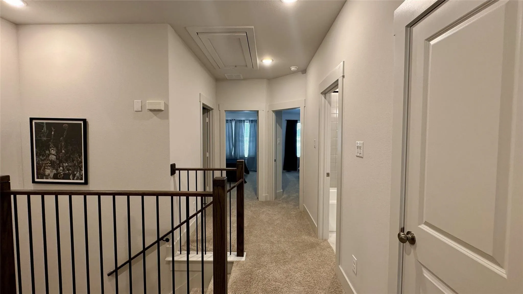 Upper-level hallway featuring plush carpeting, recessed lighting, white paneled doors, and a staircase with dark wood banisters and black metal spindles