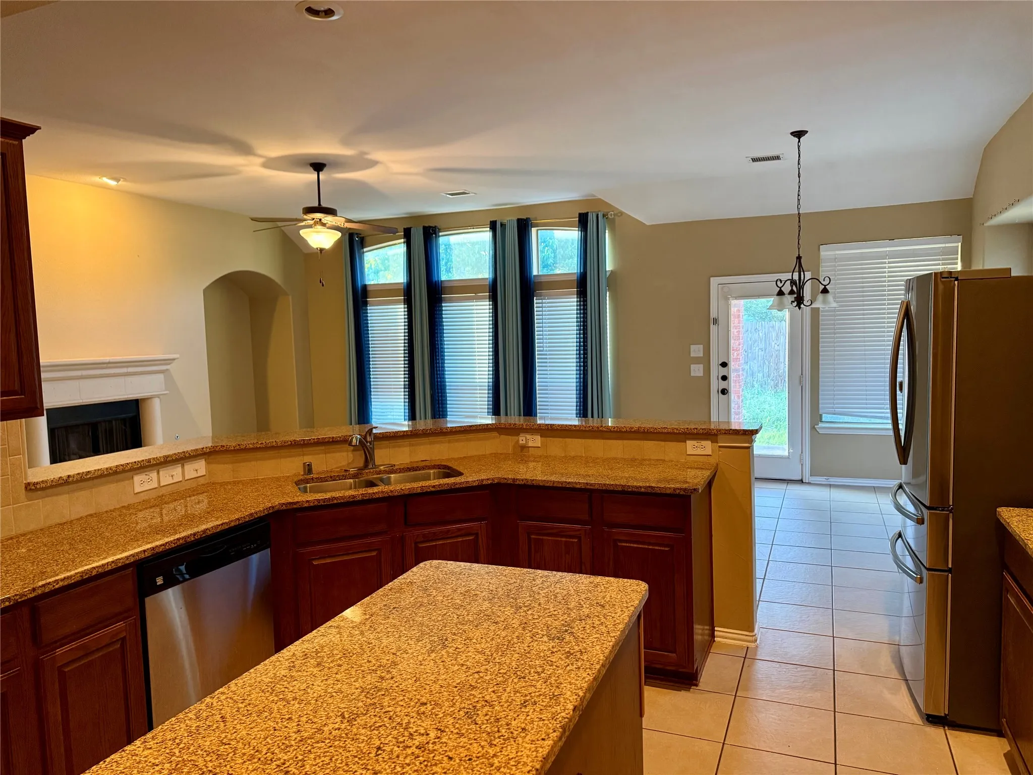 Kitchen featuring a stainless steel dishwasher, ample counter space with granite-style countertops, wood cabinetry, and an island