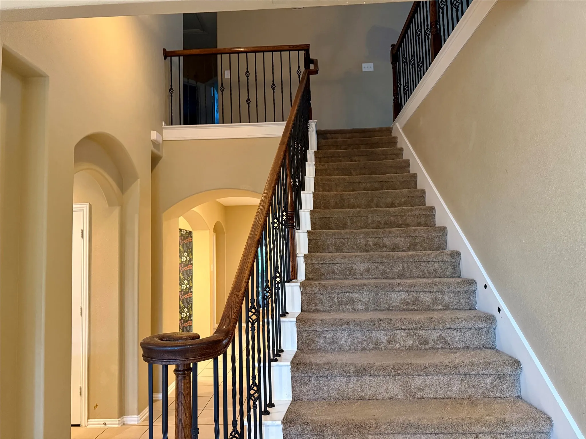 Grand staircase featuring carpeted treads, a dark wood handrail, and decorative wrought iron balusters