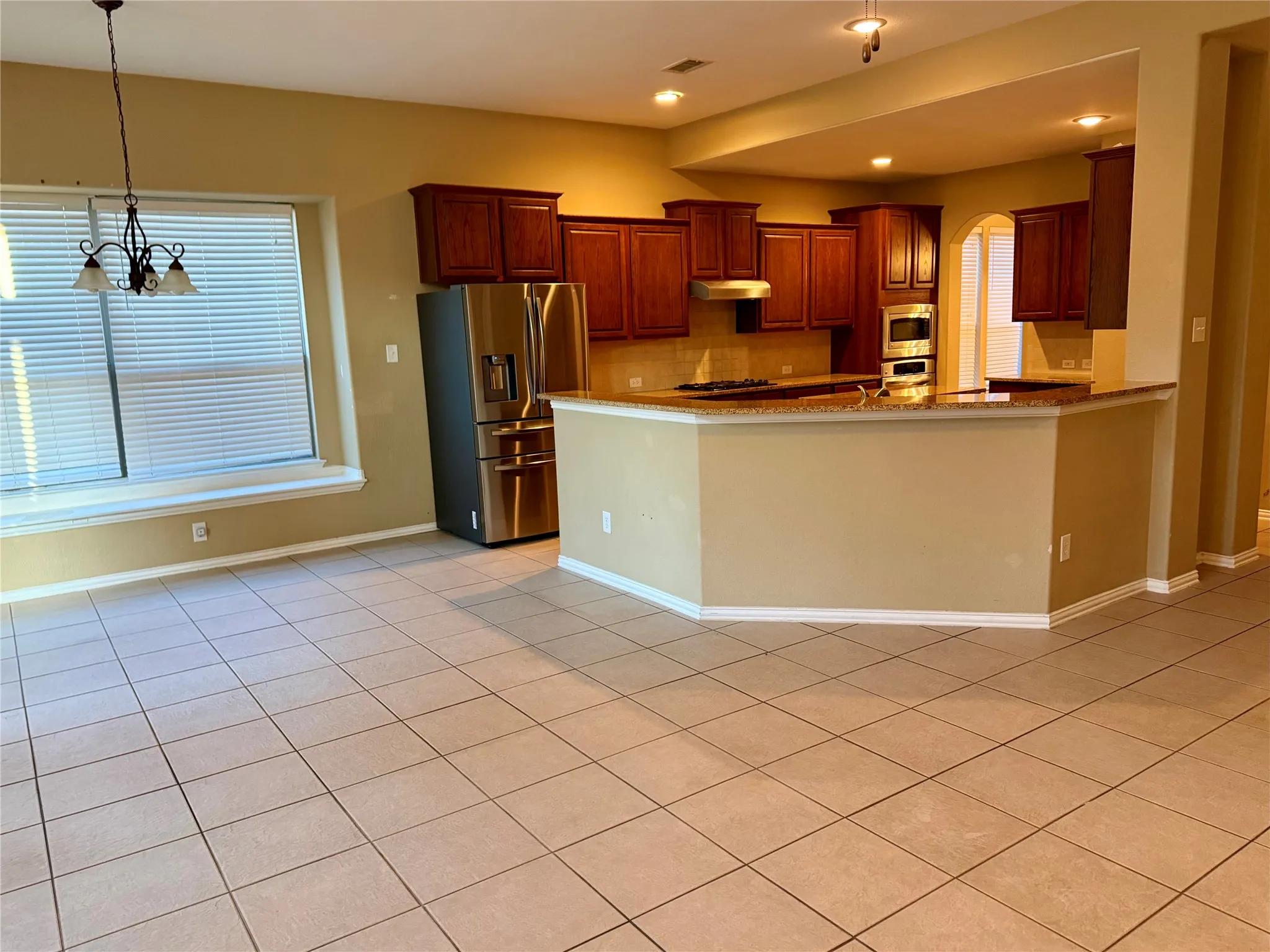 Spacious kitchen and dining area featuring tile flooring, dark wood cabinetry, stainless steel appliances, and a breakfast bar with stone countertops