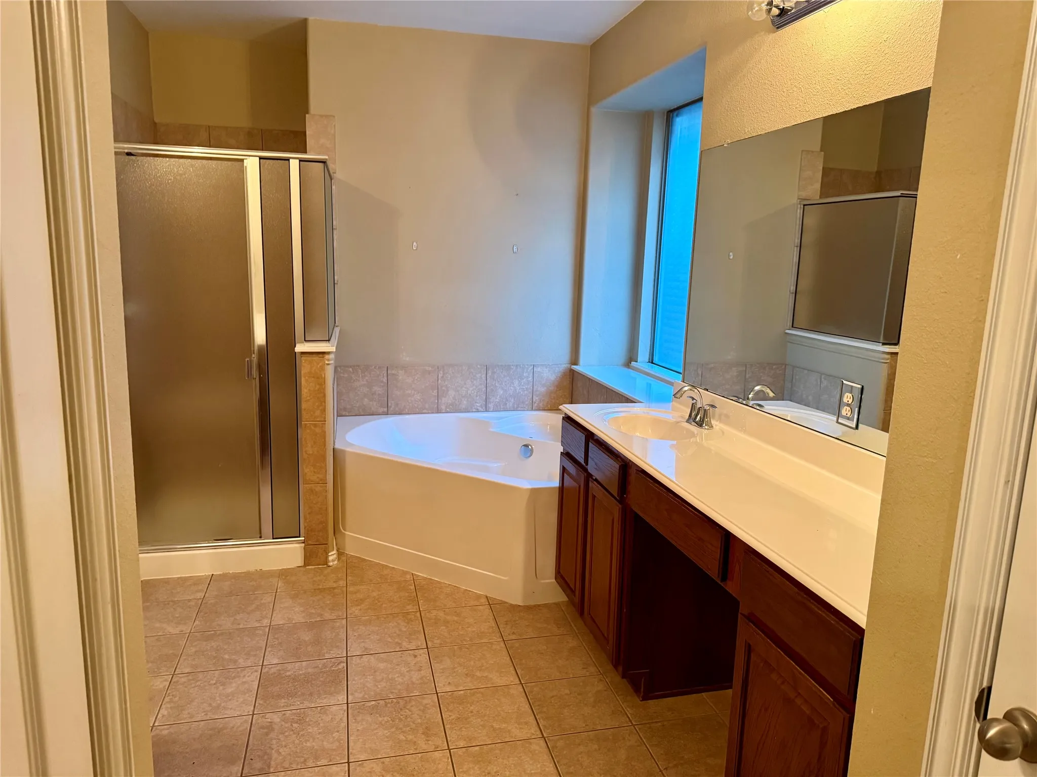 Bathroom featuring a dual vanity with integrated sinks, a corner soaking tub, and a separate glass-enclosed shower