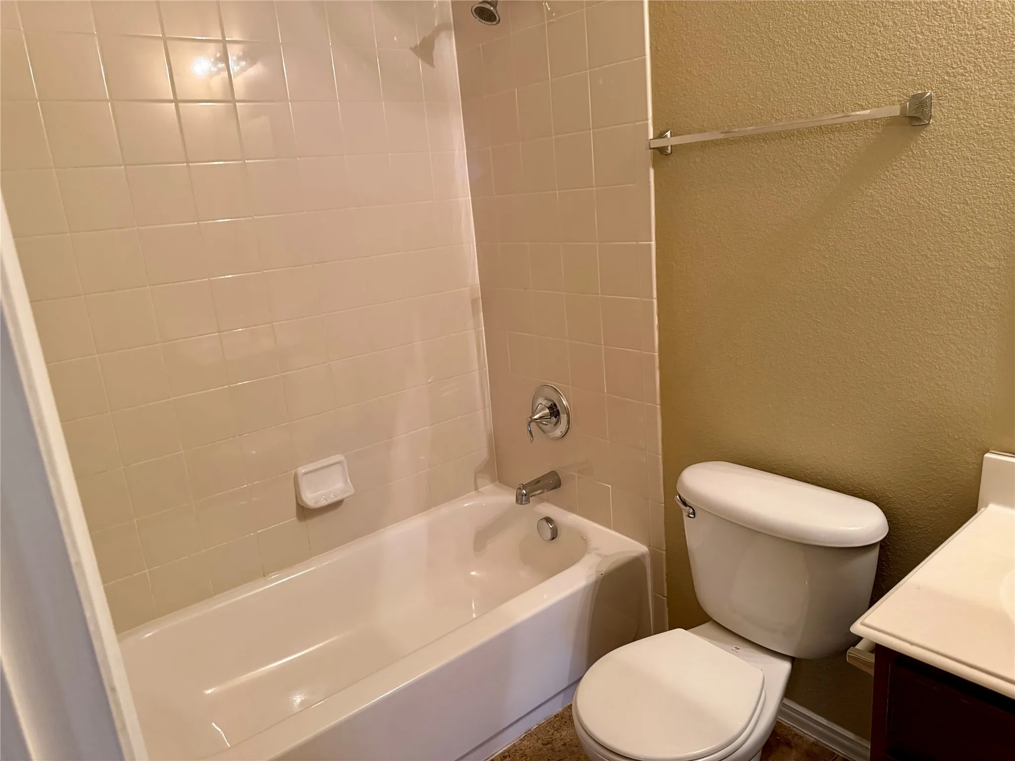 Bathroom featuring a shower-tub combination with ceramic tile surround, chrome fixtures, and a white toilet
