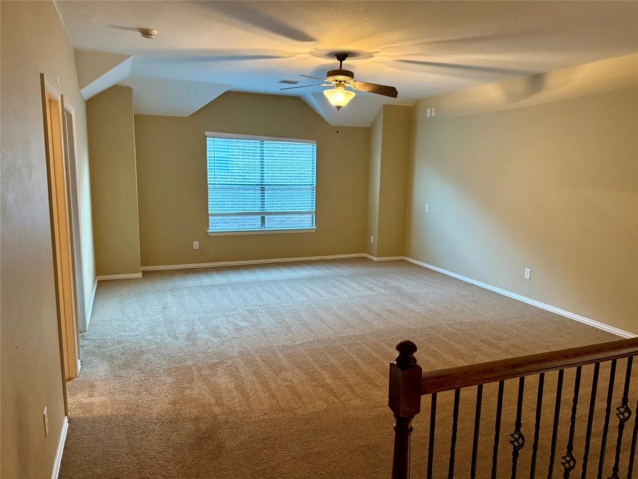 Spacious carpeted room featuring a ceiling fan with integrated lighting, multiple windows with blinds, and neutral wall tones