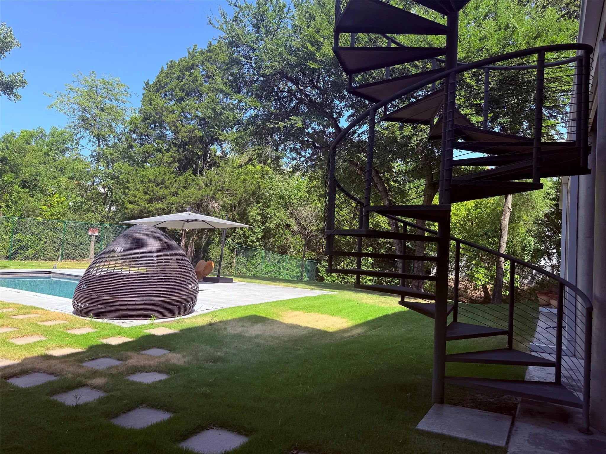 Outdoor spiral staircase, inground swimming pool, concrete pool deck, green lawn, and stepping stone pathway