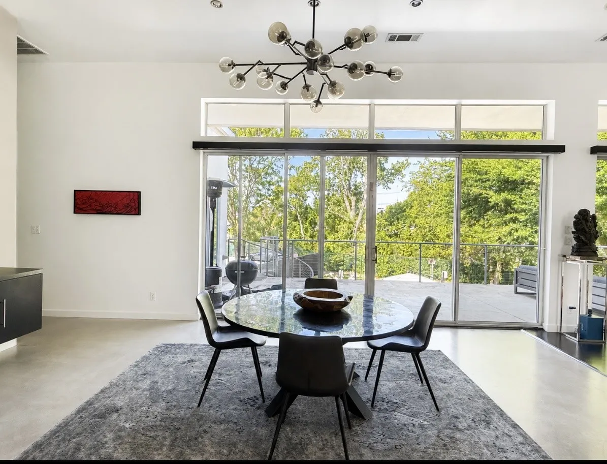 Expansive sliding glass doors, upper transom windows, modern chandelier, high ceilings, and concrete flooring