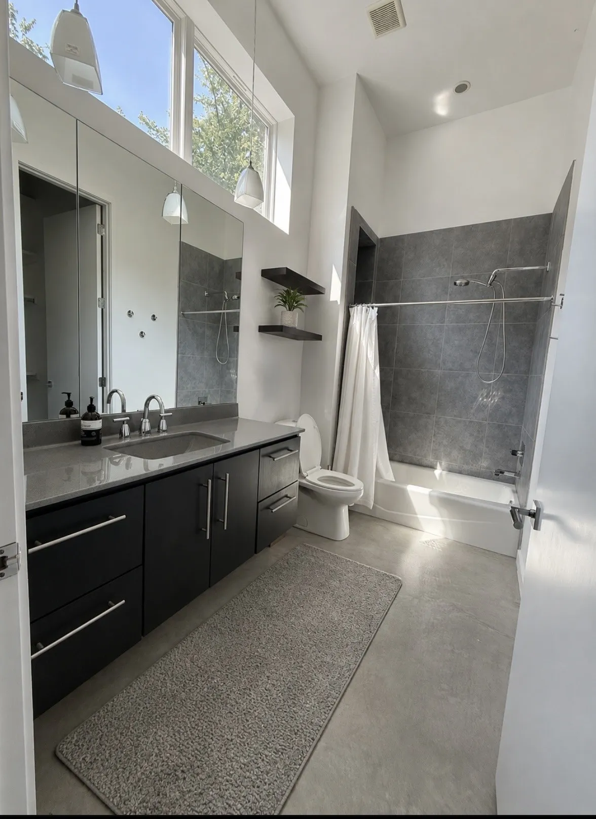 Modern bathroom featuring a dual vanity with a gray countertop, dark wood-finish cabinetry, and a bathtub with gray tile surround