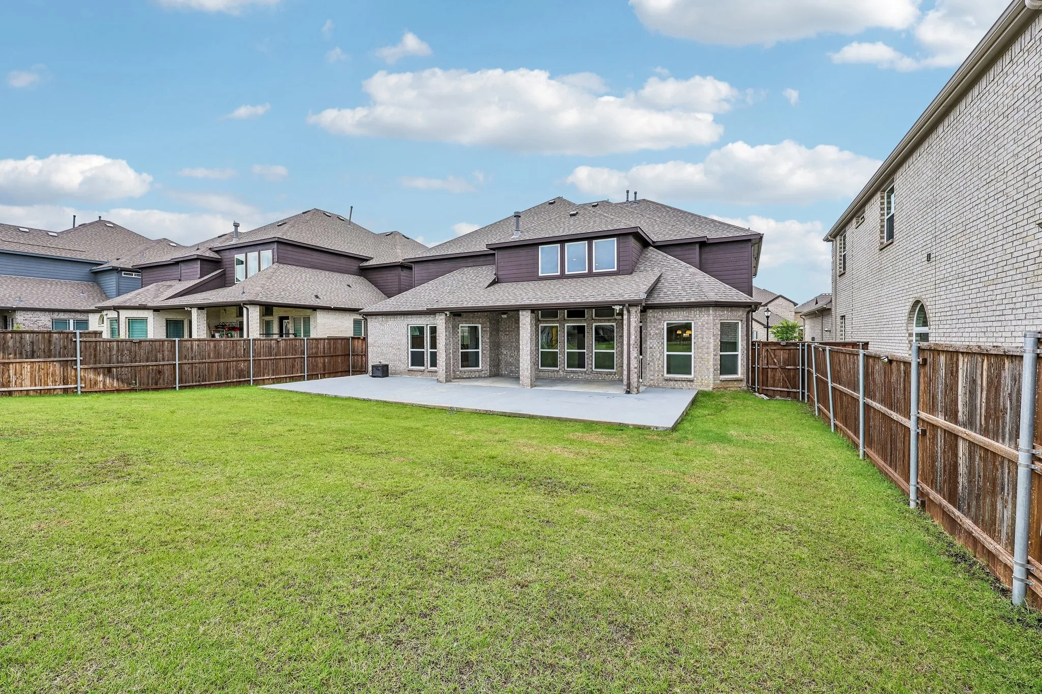 Expansive rear yard featuring a large concrete patio, abundant green lawn, and full wood privacy fencing