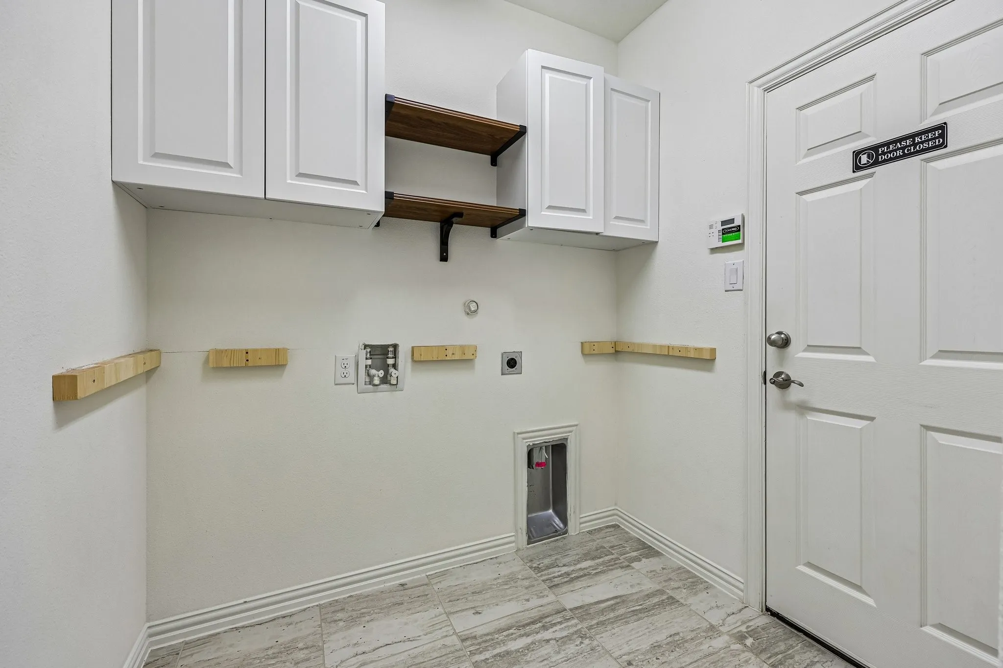Dedicated utility space featuring white shaker-style cabinetry, wood-finish open shelving, laundry hookups, and large format tile flooring
