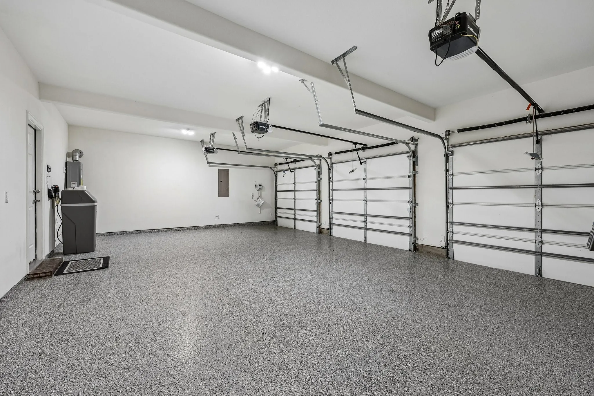 Three-car garage featuring a speckled epoxy floor coating, three overhead garage doors with automatic openers, and overhead lighting
