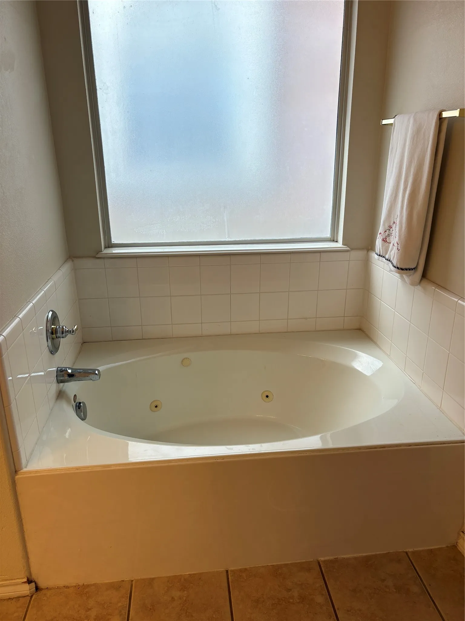 Built-in jetted tub with white tile surround and frosted privacy window