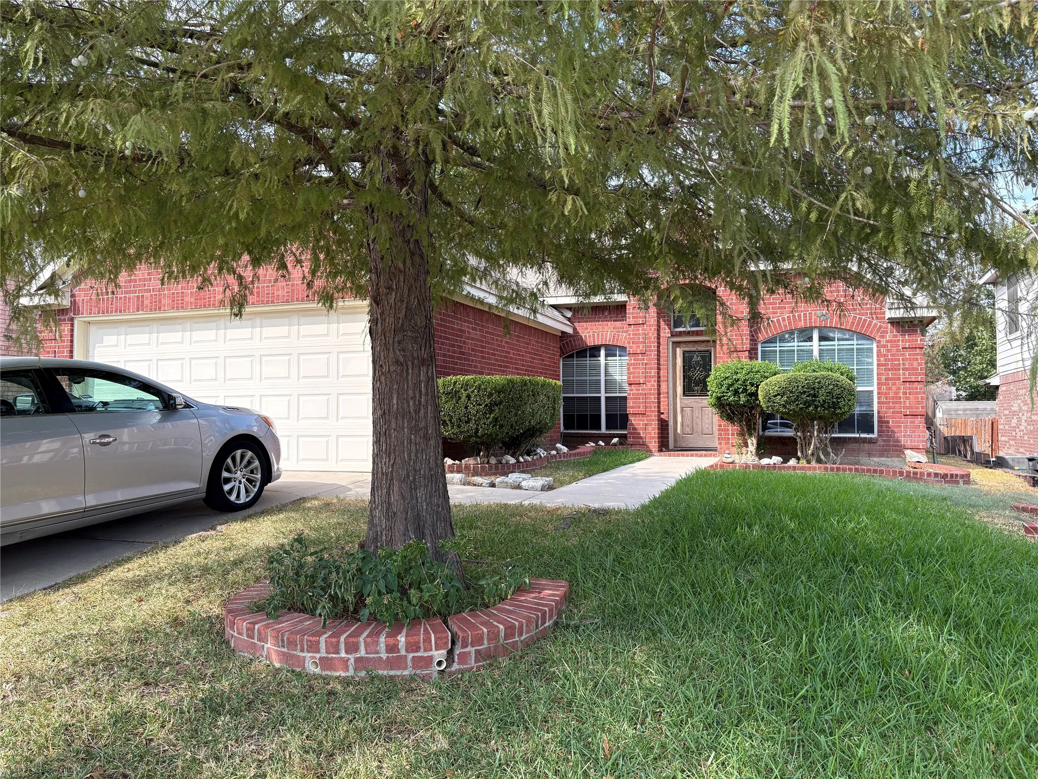 Brick exterior with arched windows, an attached garage, a mature tree, and a concrete walkway