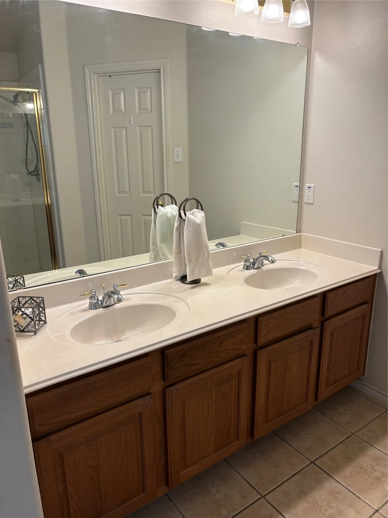 Dual under-mount sinks set into a light-toned countertop, with a full-width vanity mirror and wood-finish cabinetry