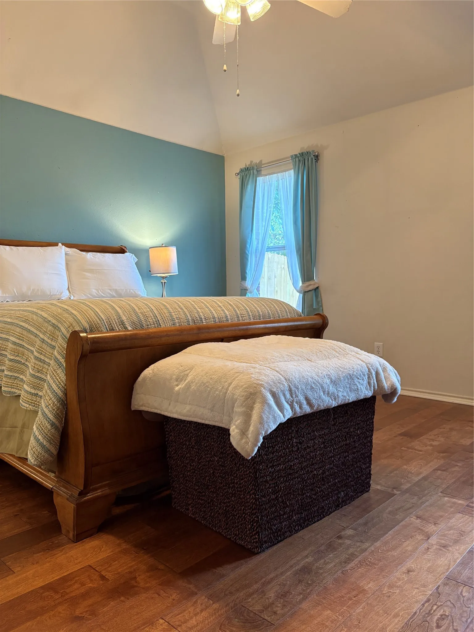 Vaulted ceiling with a ceiling fan, accent wall, wood-finish flooring, and a window with drapes
