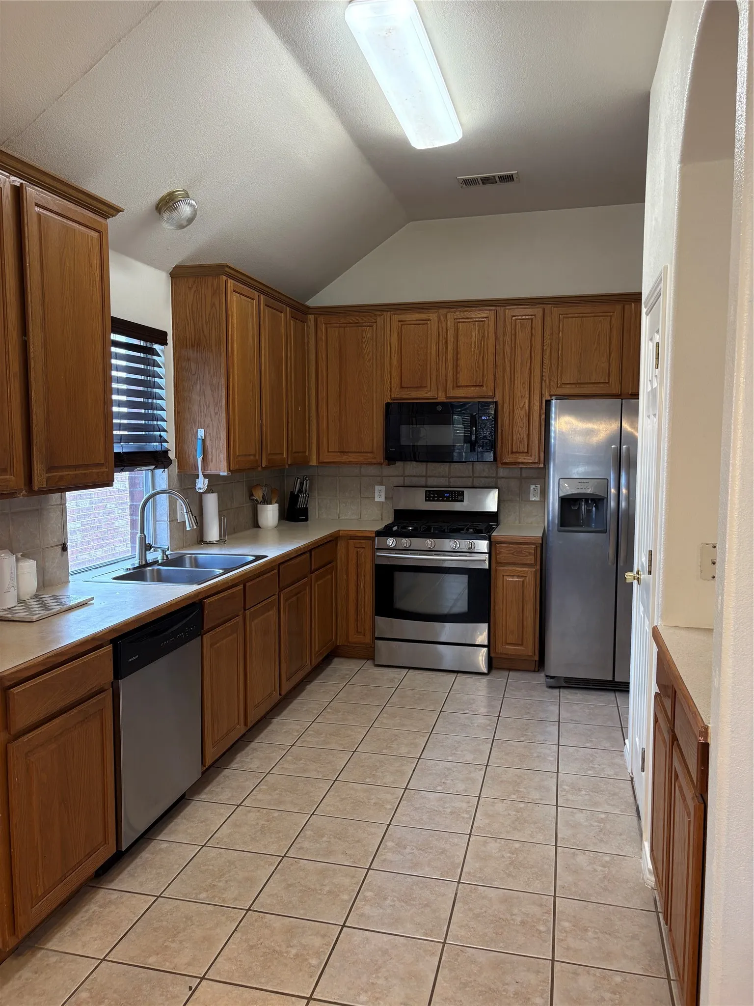 Kitchen featuring an angled ceiling, tile flooring, wood-finish cabinetry, stainless steel appliances, and solid surface countertops