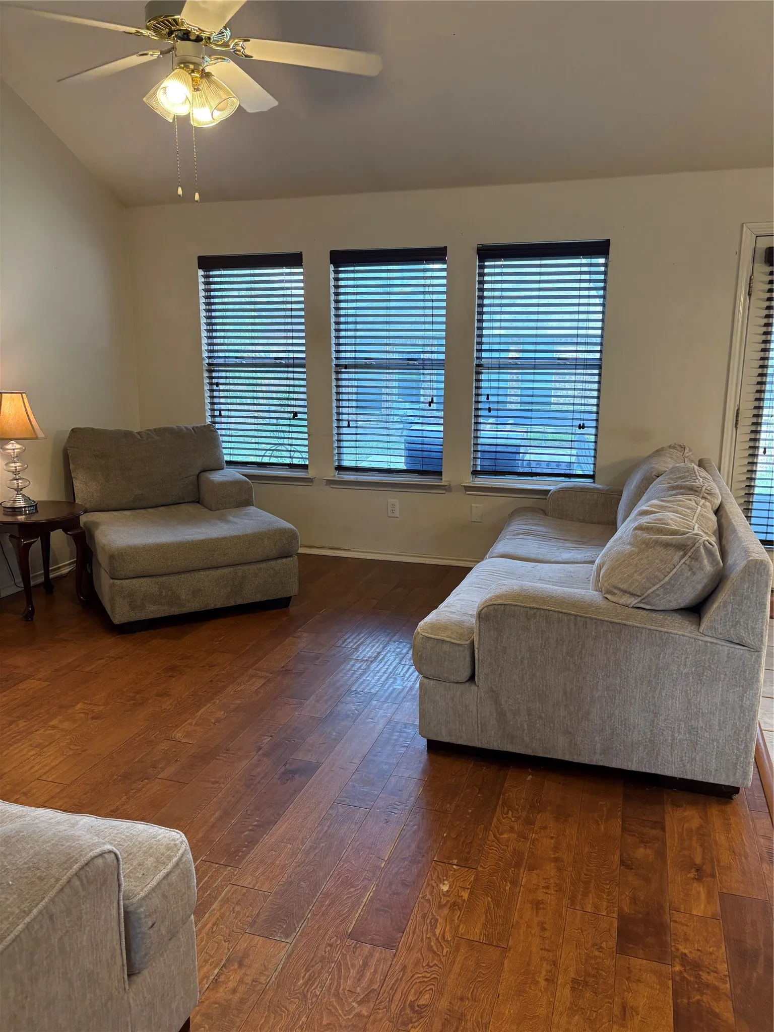 Vaulted ceiling with a ceiling fan, three windows with blinds, and wood-finish flooring