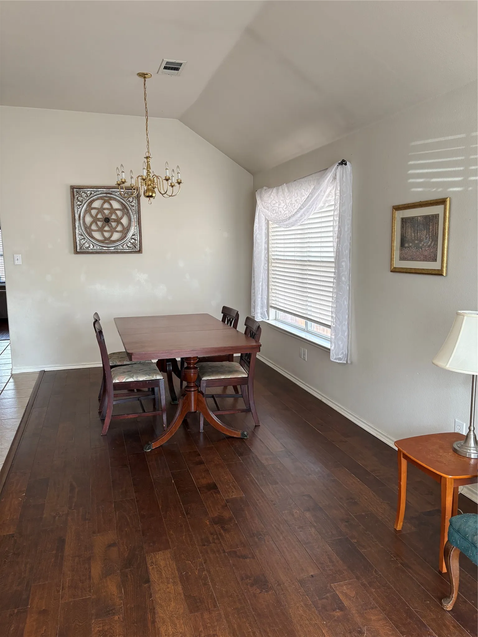 Vaulted ceiling with an attached chandelier, wood-finish flooring, and a single window with blinds