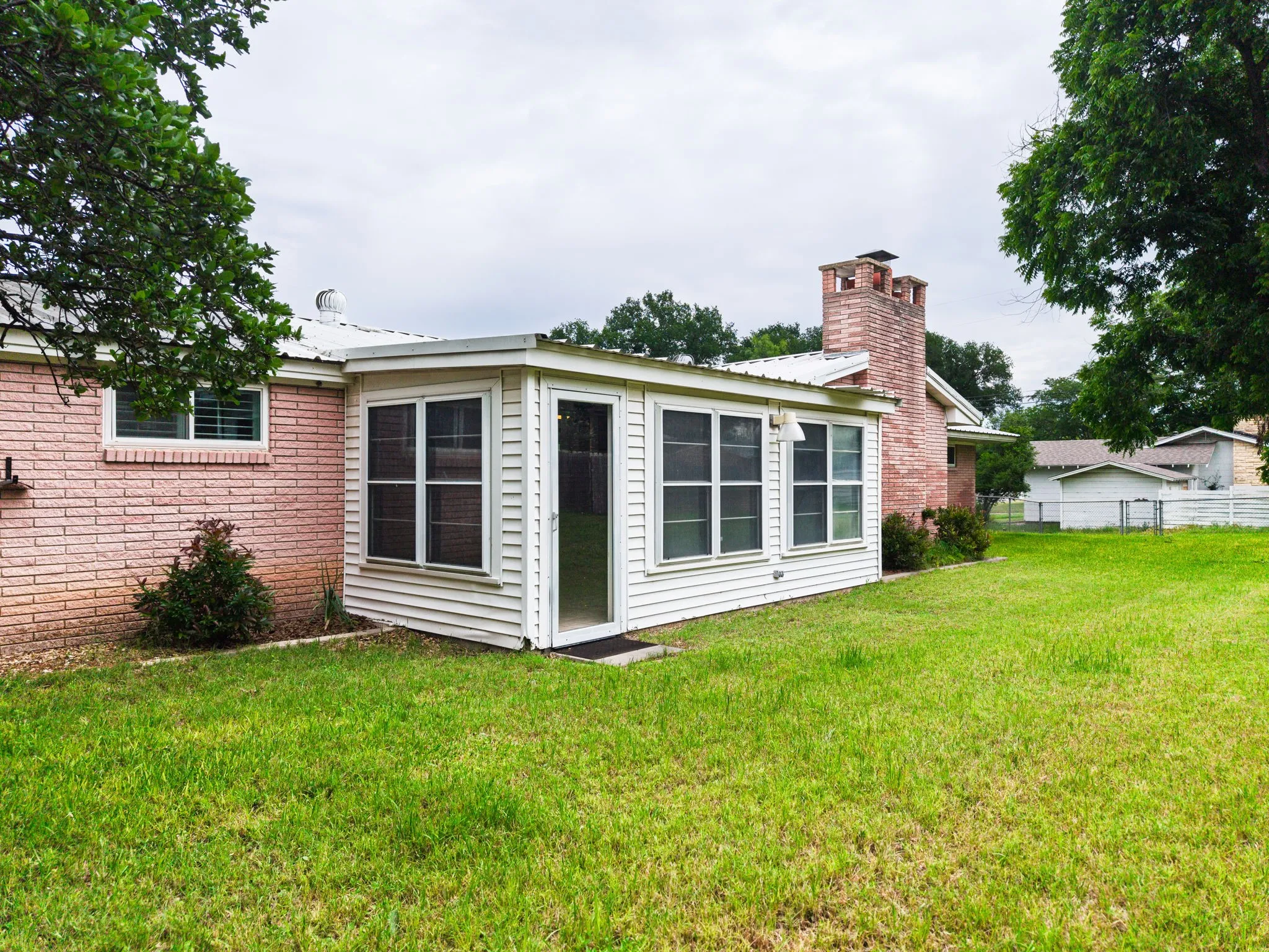 Expansive backyard featuring a manicured lawn, a detached screened enclosure, and a brick exterior with a prominent brick chimney