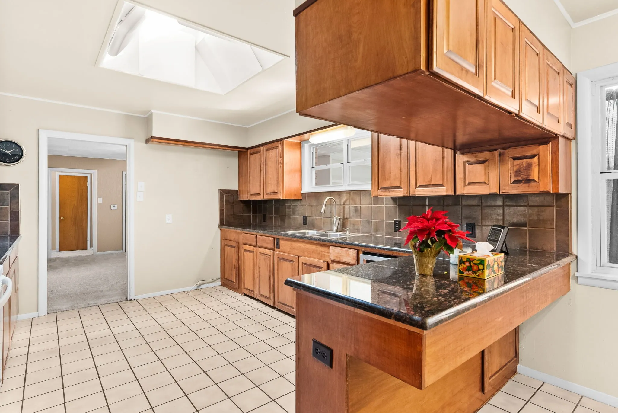 Kitchen featuring a skylight, wood cabinetry, dark countertops, a tile backsplash, and tile flooring