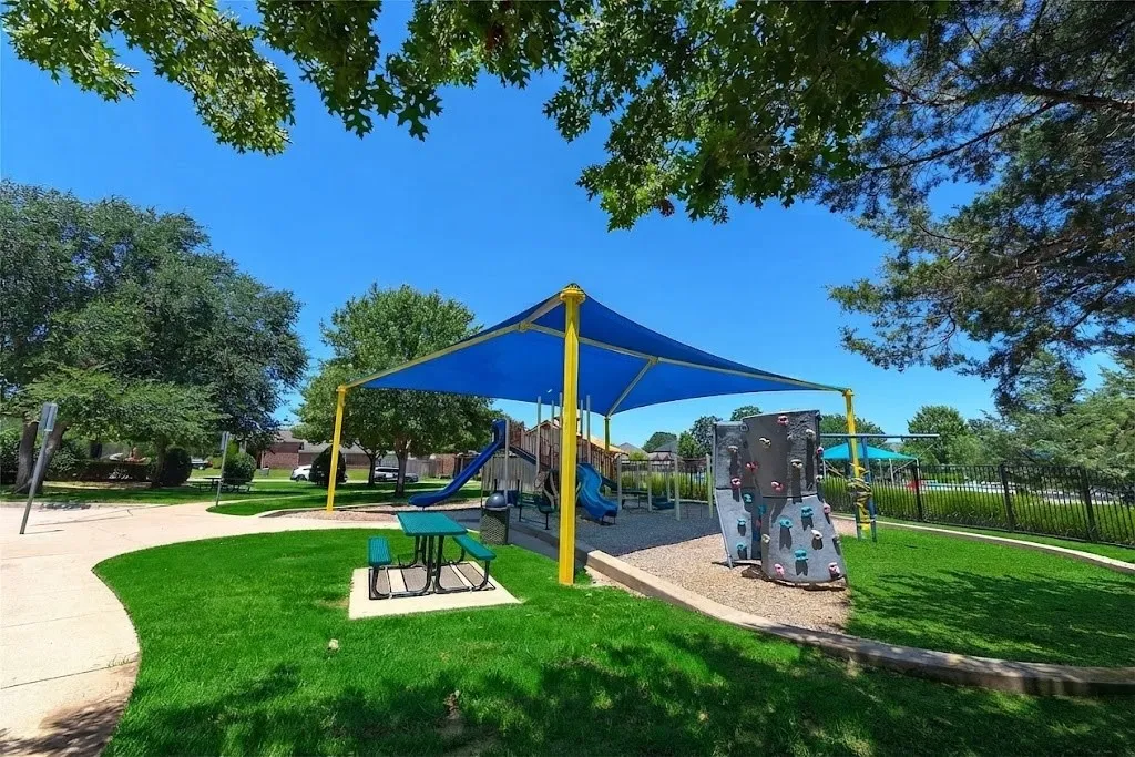 Playground area featuring a blue shade structure, rock climbing wall, and picnic seating