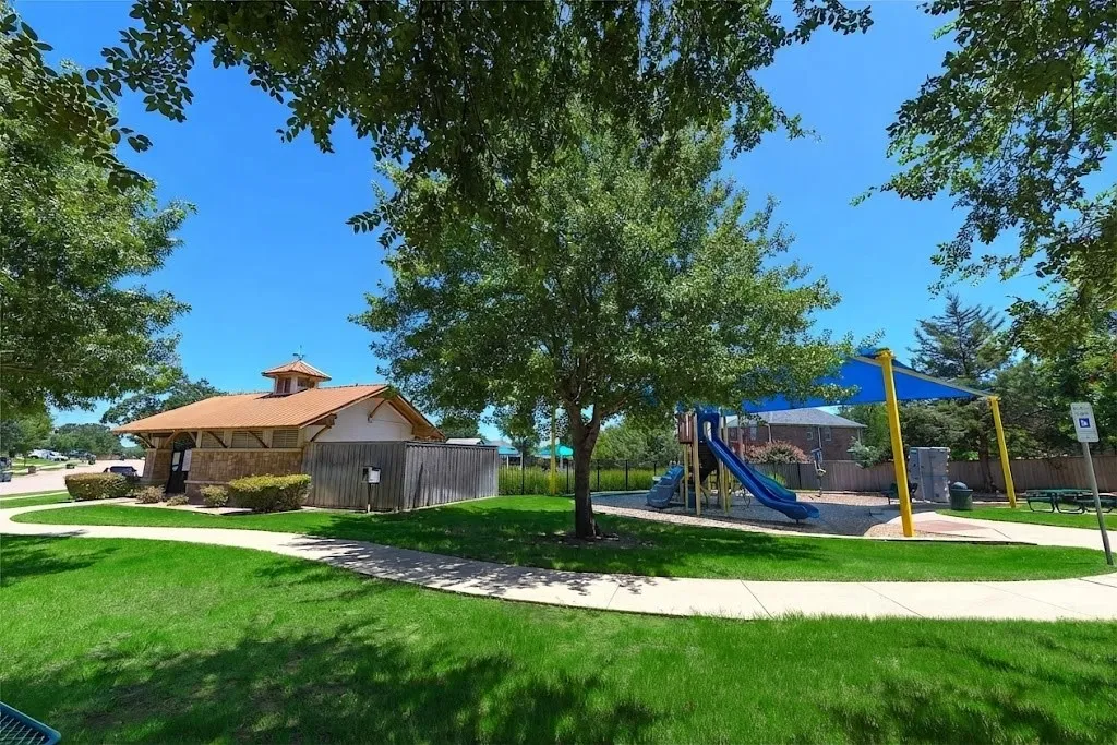 Manicured green spaces with mature trees, a covered playground, and a stone-accented building with a cupola