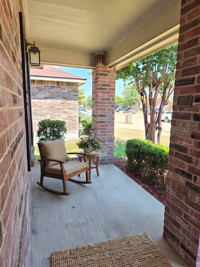 Covered front porch featuring brick columns and exterior wall, concrete flooring, and an attached outdoor light fixture