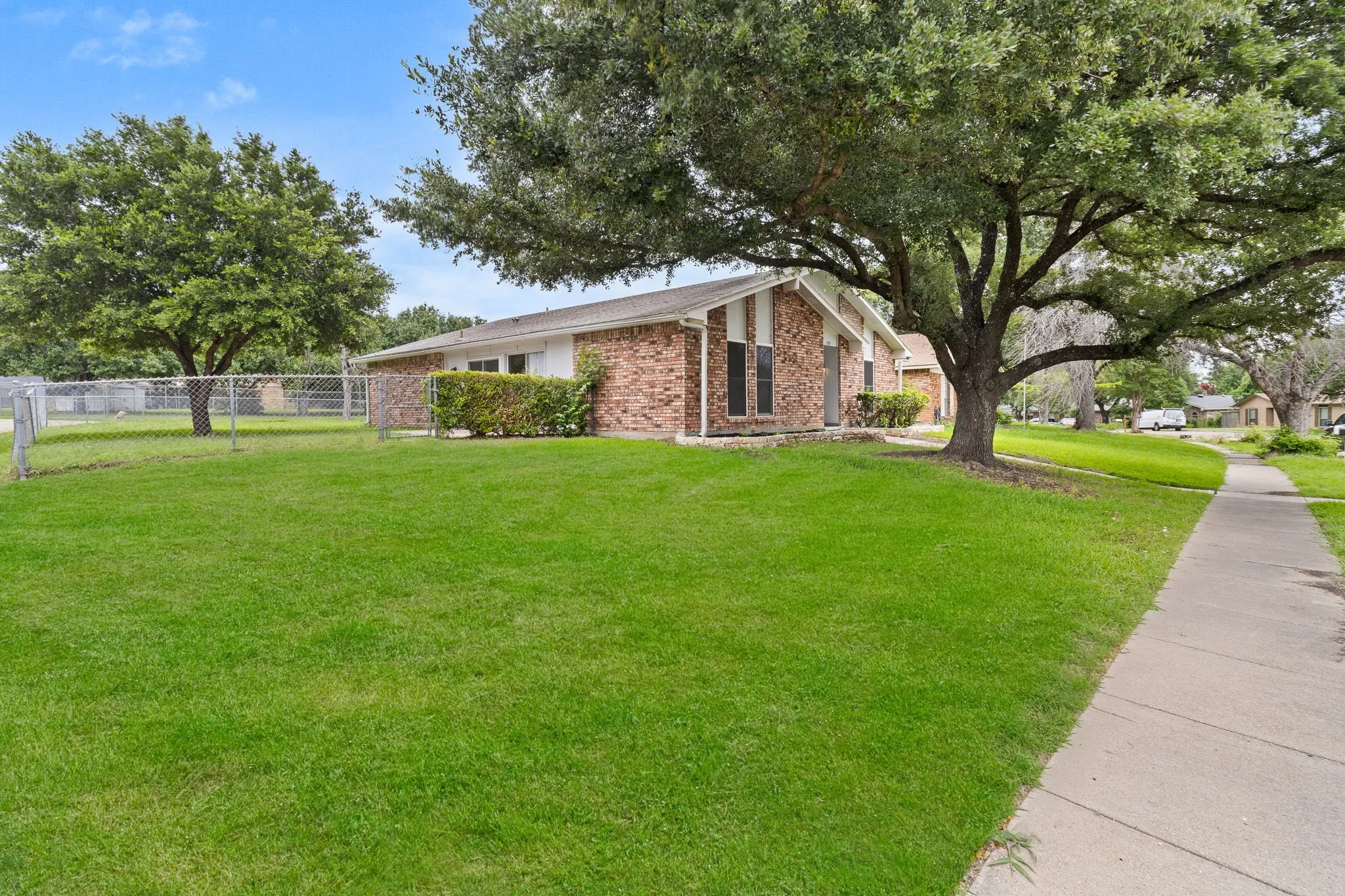 Brick exterior residence featuring a substantial tree and a sidewalk