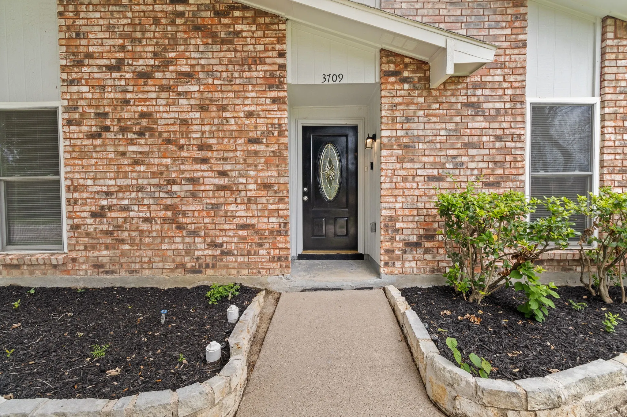 Brick exterior with white trim, featuring a dark front door with oval glass insert and sidelight