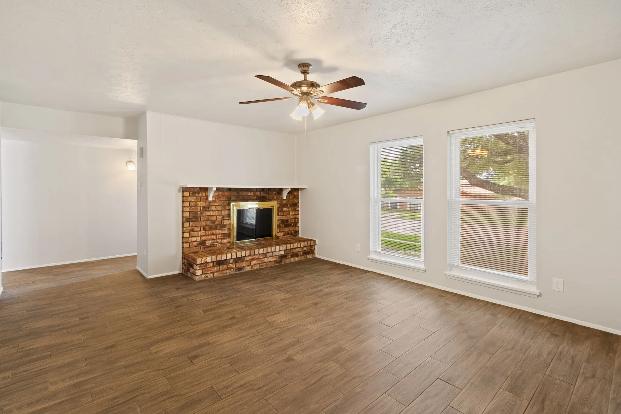 Spacious room featuring wood-finish flooring, a brick fireplace with a white mantel, and two windows providing natural light