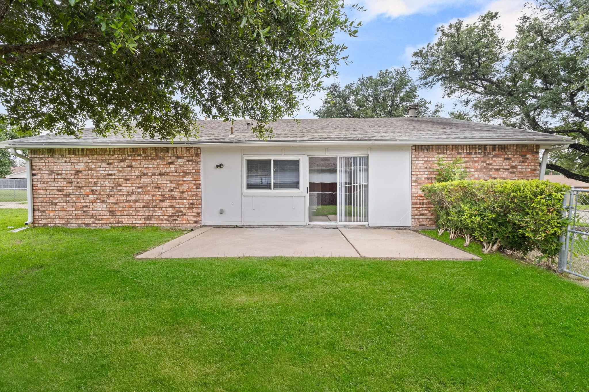 Expansive backyard featuring a concrete patio, a sliding glass door, and brick and siding exterior