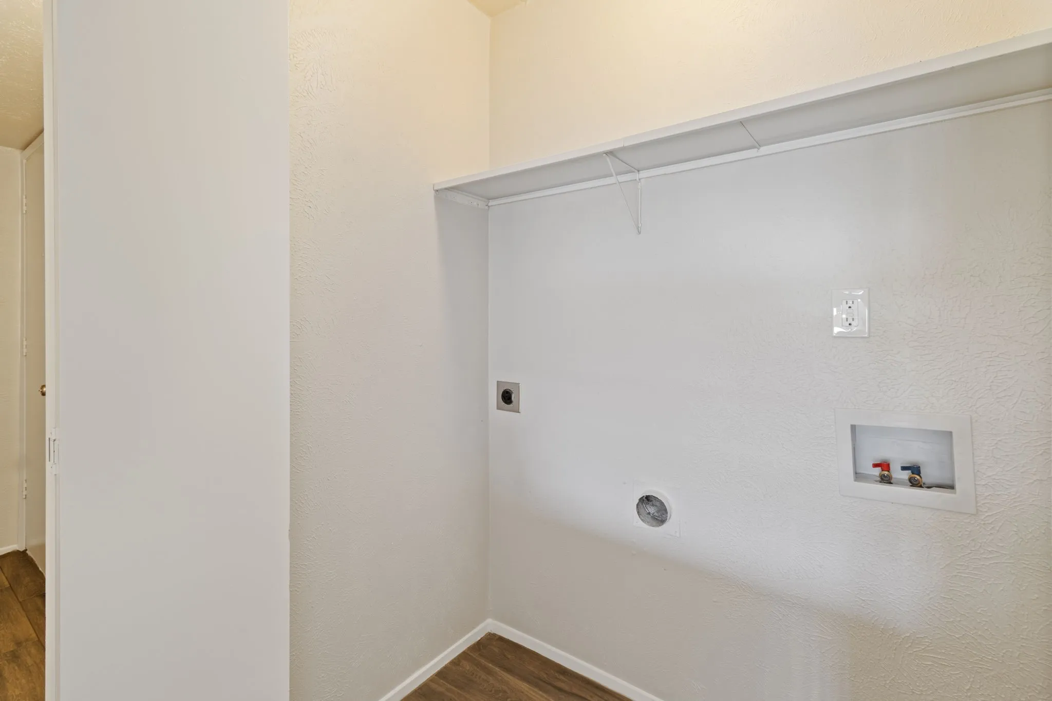Dedicated laundry area featuring a built-in wire shelf, wood-finish flooring, and essential utility hookups