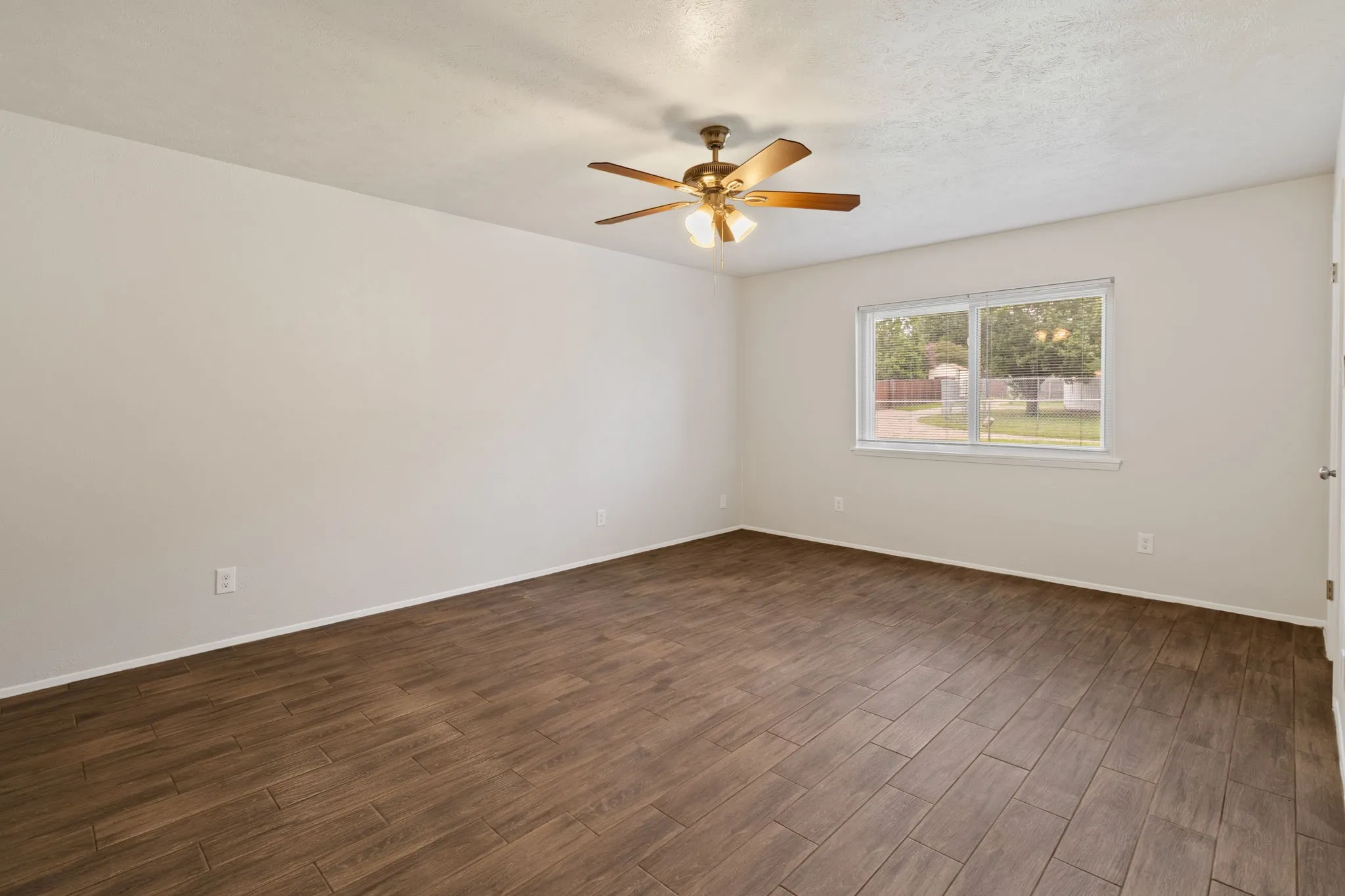 Spacious room featuring wood-finish flooring, light-toned walls, and a ceiling fan with integrated lighting