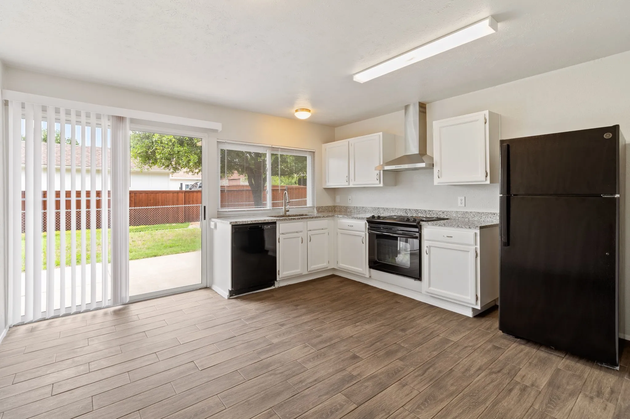 Kitchen featuring white cabinetry, black appliances, speckled countertops, and wood-finish flooring