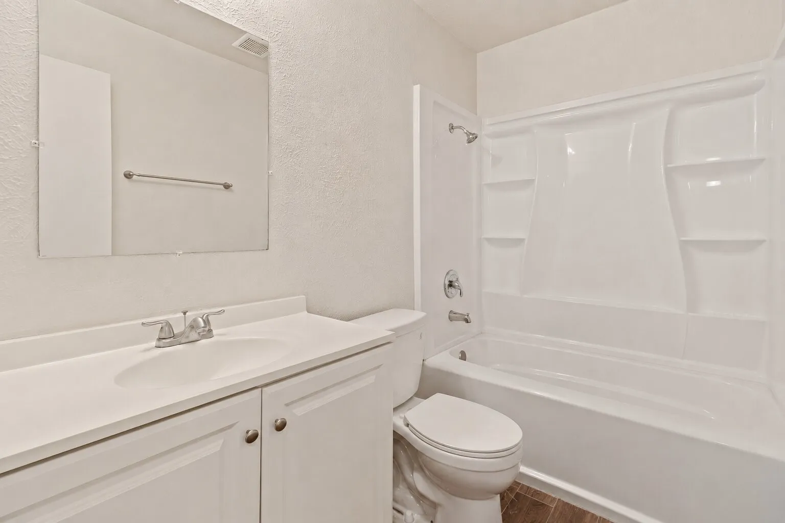 Bathroom featuring a white vanity with integrated sink, chrome faucet, white cabinetry, and a white tub/shower combination with built-in shelving