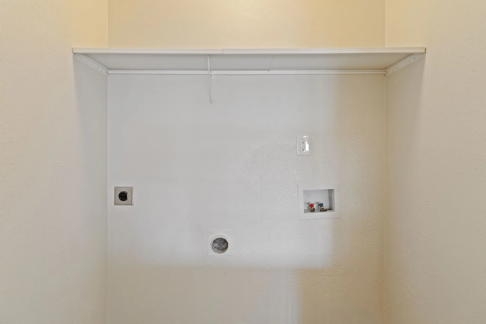 Dedicated laundry area featuring a built-in shelf, clothing rod, electrical outlet, dryer vent, and water hookups